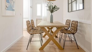 A dining area with a wooden table, four wicker chairs, a vase with greenery, and a hanging light fixture. - Avenida América - Comfortable apartment, next to the station (Madrid)