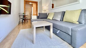 Ein modernes Wohnzimmer mit einem grauen Sofa, einem Holztisch und einem kleinen Essbereich mit Tisch und Stühlen.