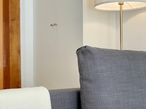 Un canapé gris surmonté d’un plaid blanc, une porte fermée et un lampadaire.
