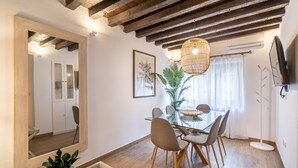 Een eetgedeelte met een glazen tafel, houten stoelen, een hanglamp en een grote spiegel.