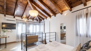 Een slaapkamer met een houten plafond, een bed met witte lakens, een nachtkastje, een spiegel en een raam met dunne gordijnen.