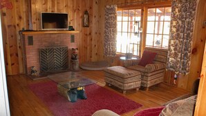Ein gemütliches Wohnzimmer mit Kamin, einem Glastisch, einer Couch und einem gemusterten Sessel.