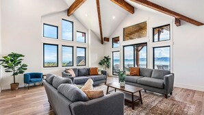 A spacious living room with large windows, a high ceiling with exposed beams, and a view of the outdoors.