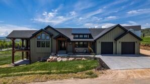 A modern two-story house with a covered patio, a garage, and a well-maintained lawn.