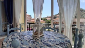 A balcony with a table covered in a blue and white fish pattern tablecloth, a white lantern, and a view of buildings and greenery in the background. - Apartment "La Veranda": the beaches of San Lorenzo al Mare just a few steps away (San Lorenzo al Mare)