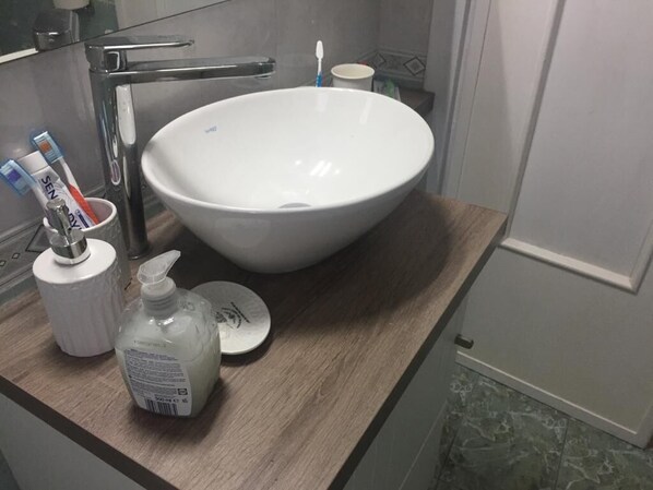Un baño con un lavamanos grande de color blanco, un portacepillos de dientes y una botella de jabón líquido sobre la encimera.