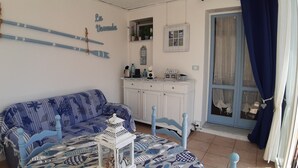 A room with a blue sofa, a small table with a fish-patterned tablecloth, a white cabinet, and a window with curtains. - Apartment "La Veranda": the beaches of San Lorenzo al Mare just a few steps away (San Lorenzo al Mare)