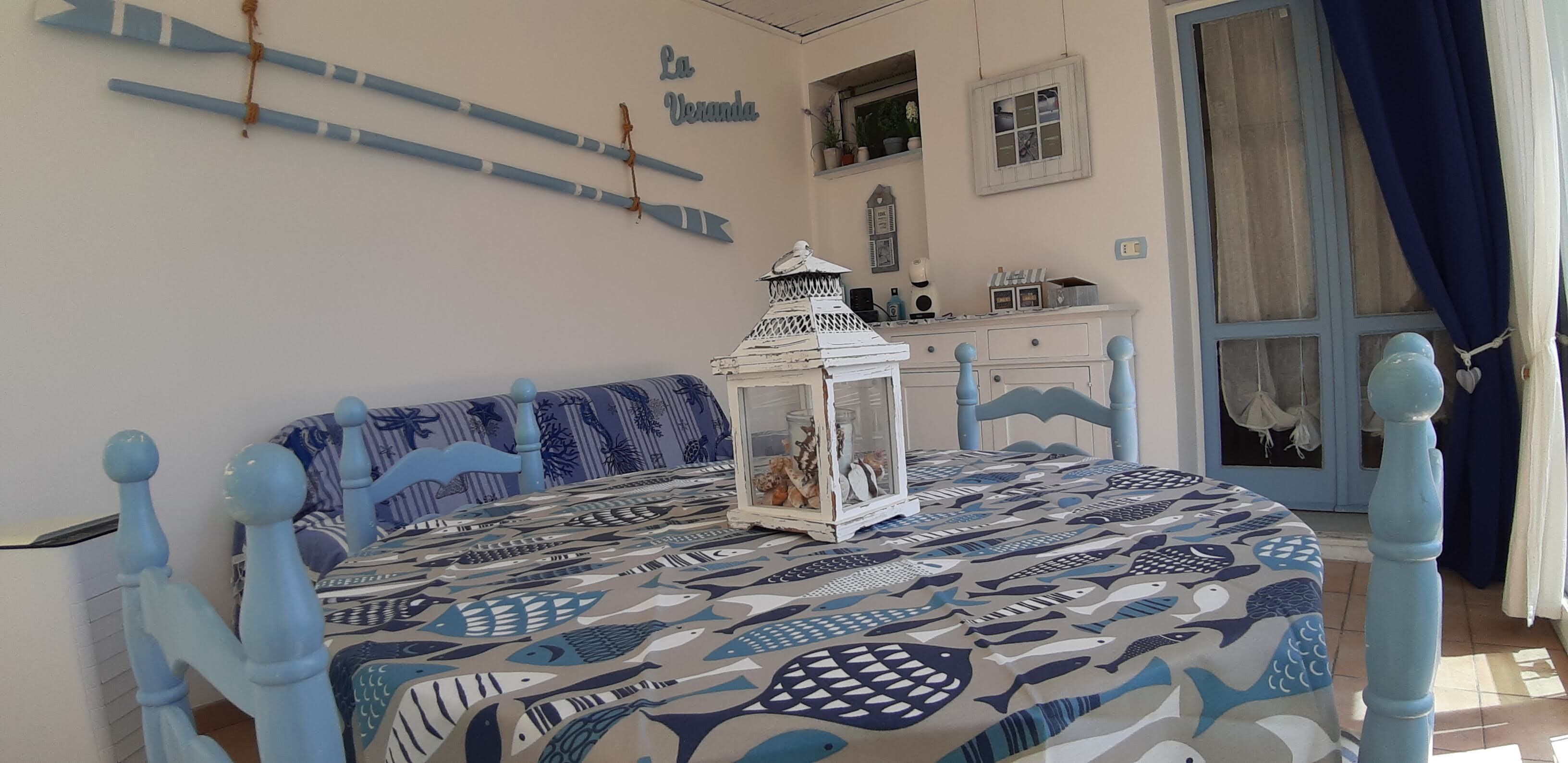 Habitación con una cama y una colcha azul y blanca con motivos náuticos, una mesita de noche blanca con un farol decorativo y un tocador con objetos pequeños encima.