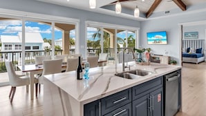 A modern kitchen with a large island, a dining area with chairs, and a view of the ocean. - Elev • 5BR/8BA • Game Room • 75’ Deep Canal Dock • Ice Maker • Kayaks • Bikes (Key Colony Beach)