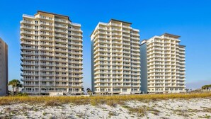 Three high-rise buildings with balconies, situated on a sandy beach with sparse vegetation. - Sky Meets The Sea: Stunning 11th Floor Unit in Summerwind West! (Navarre Beach)