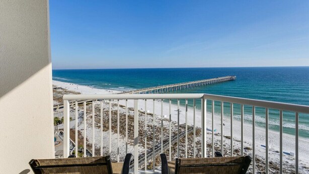 A balcony with a view of a beach and a pier. - Sky Meets The Sea: Stunning 11th Floor Unit in Summerwind West! (Navarre Beach)