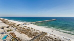 A beach with a long pier extending into the ocean, a swimming pool, and a sandy area with lounge chairs. - Sky Meets The Sea: Stunning 11th Floor Unit in Summerwind West! (Navarre Beach)