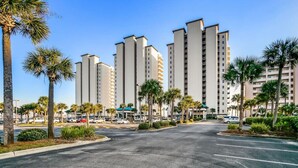 A parking lot with multiple high-rise buildings in the background, surrounded by palm trees. - Sky Meets The Sea: Stunning 11th Floor Unit in Summerwind West! (Navarre Beach)