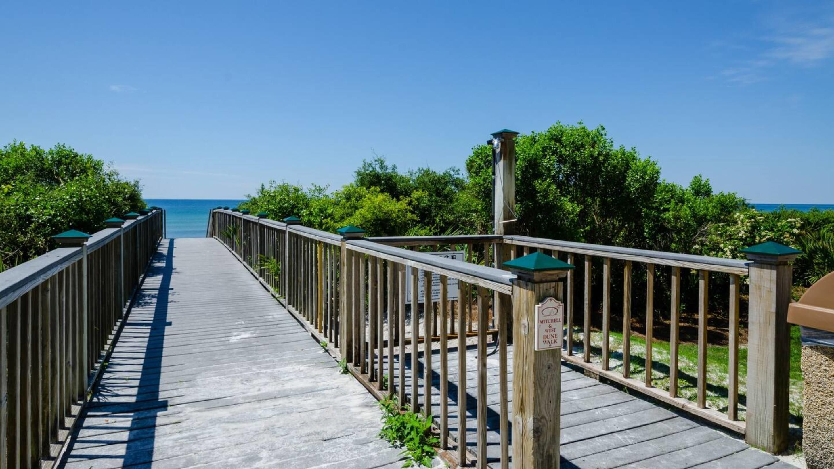 Ein hölzerner Boardwalk führt zu einem Strand, an dem ein Schild 'Mitchell & West Dune Walk' steht.