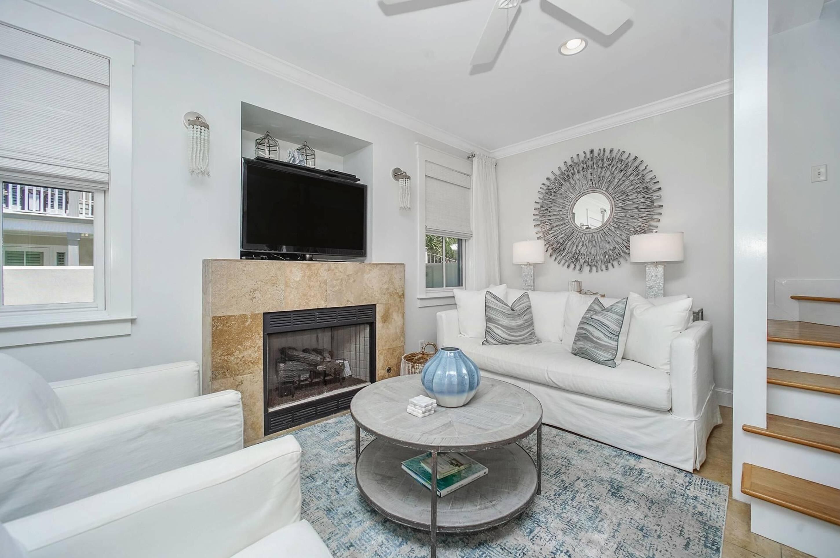 A modern living room with a fireplace, white furniture, a round coffee table, and a television mounted above the fireplace.