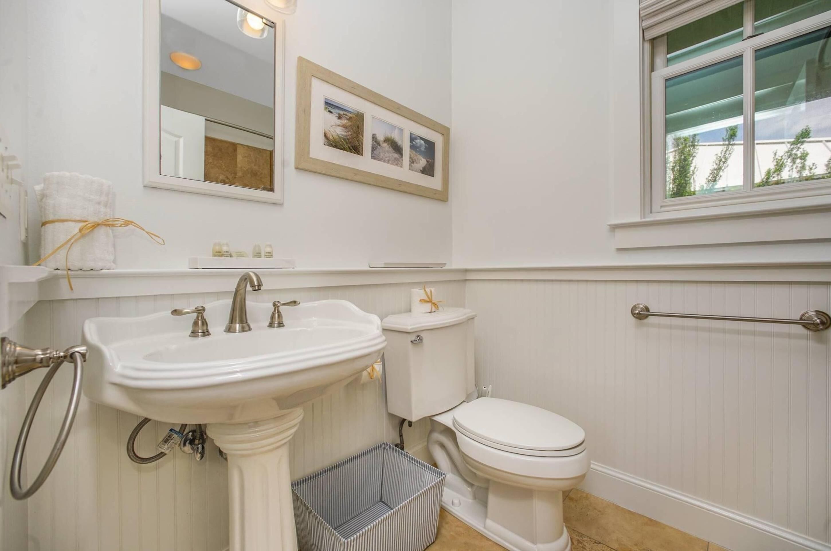 A bathroom with a pedestal sink, toilet, and a window with a view of greenery.