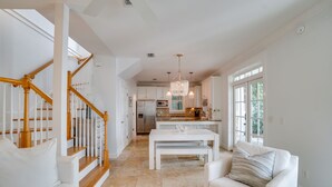 A spacious living area with a staircase, a dining table, and a kitchen in the background. - 30A Beach House - Stillwater Cottage By Panhandle Getaways (Panama City Beach)