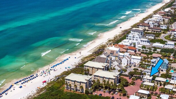 An aerial view of a coastal area with a beach, a row of white buildings, and a blue arrow pointing to a specific location. - 30A Beach House - Stillwater Cottage By Panhandle Getaways (Panama City Beach)