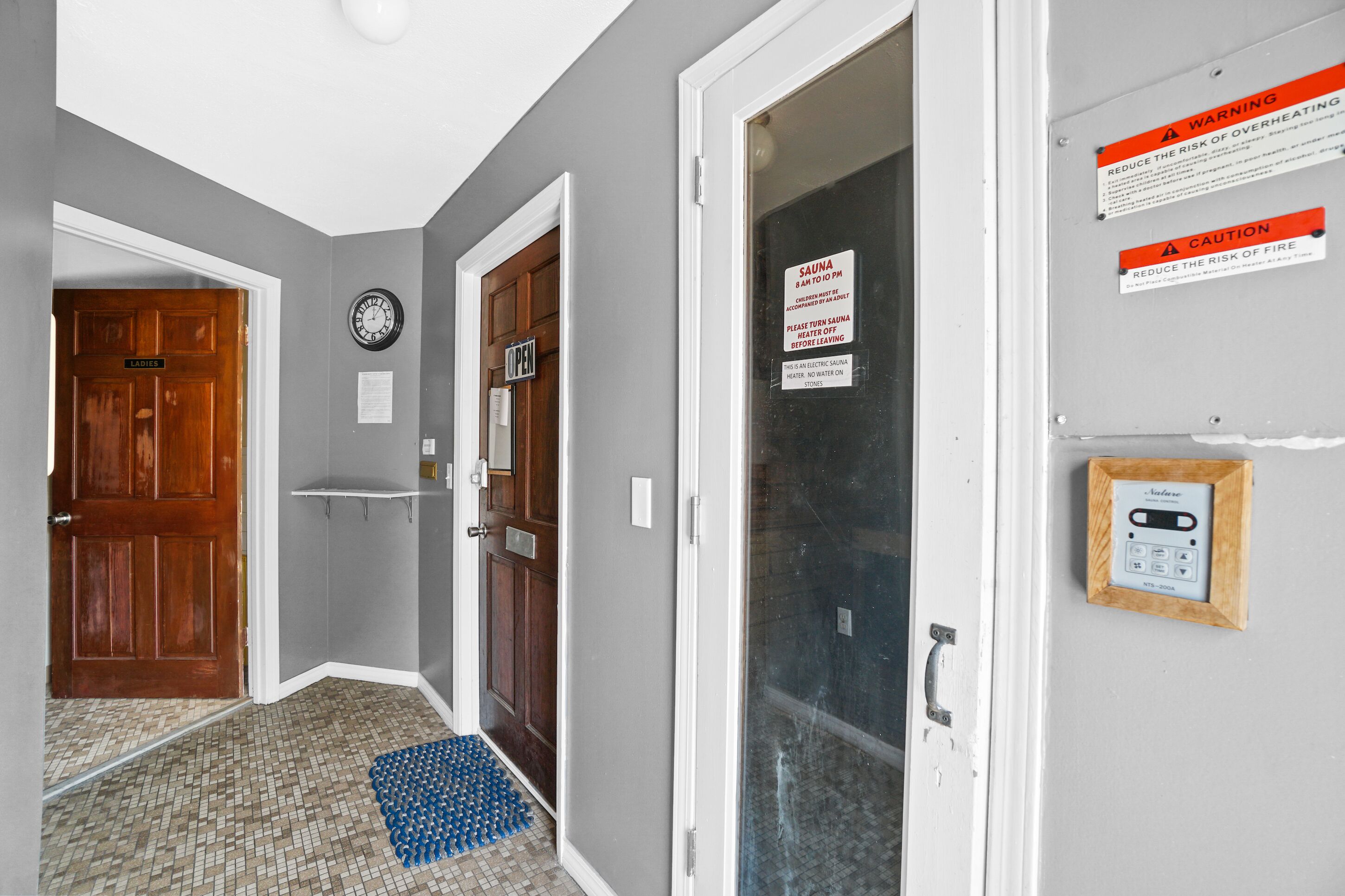 A hallway with a wooden door labeled "Ladies," a clock, and a sauna sign.