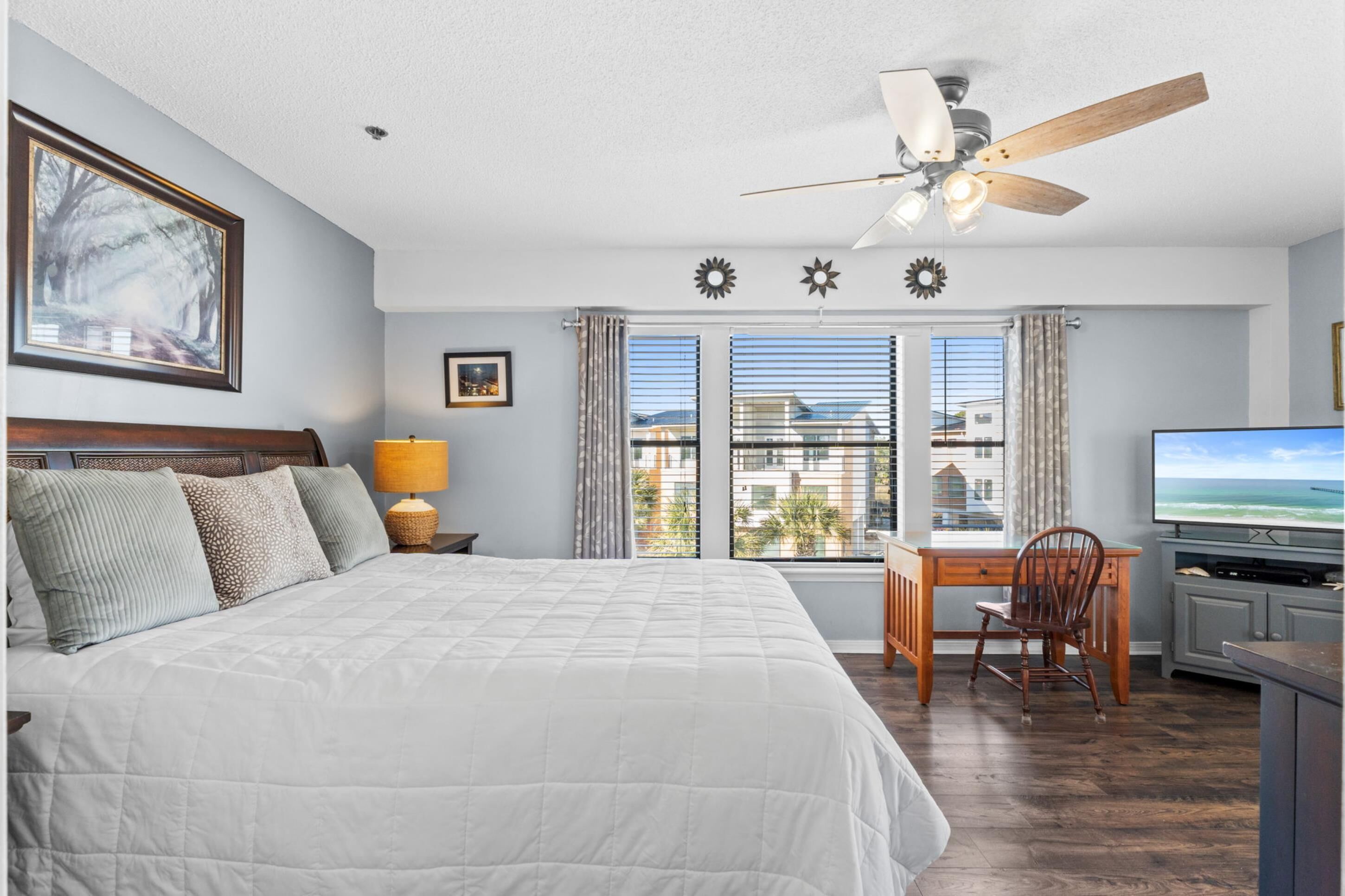 A bedroom with a bed, a desk, a chair, a television, and a ceiling fan.