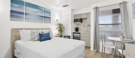 A bedroom with a bed, a desk, and a kitchenette.