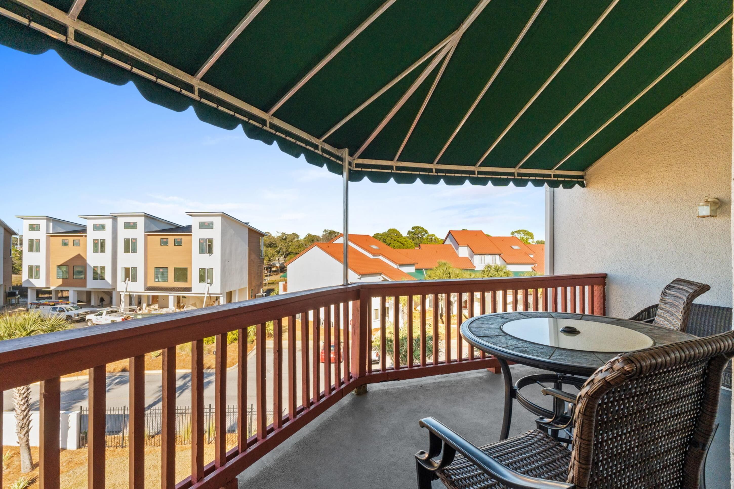A balcony with a table and chairs, overlooking a street with buildings and parked cars.
