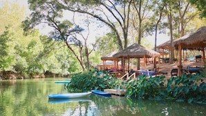A serene riverside setting with thatched-roof huts and wooden benches along the water's edge.