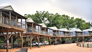 Una estructura rústica de madera con varios niveles, asientos al aire libre y suelo de tierra.