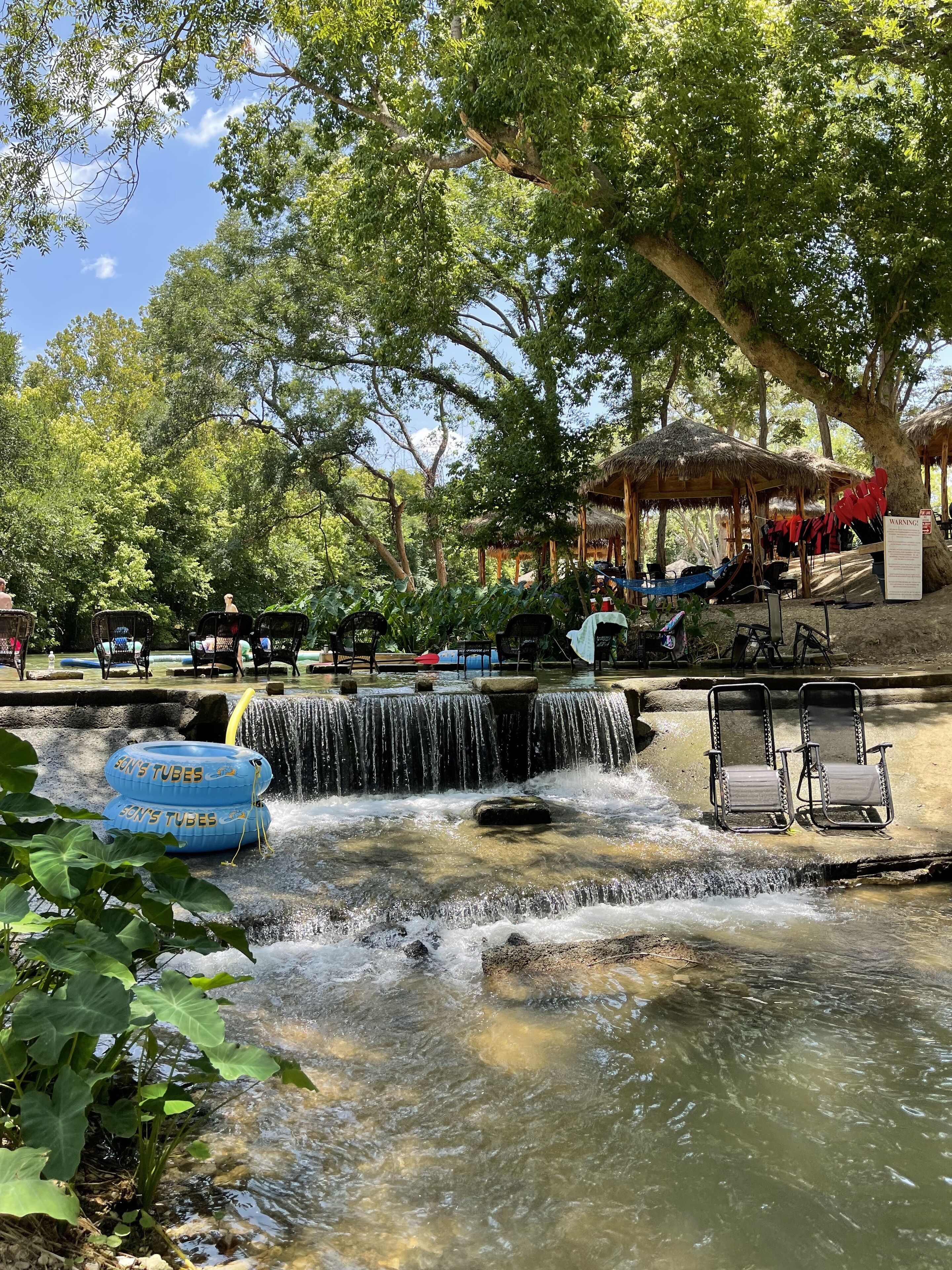A water feature with a small waterfall, surrounded by trees and a gazebo.