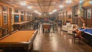 Un grand espace intérieur aménagé avec plusieurs tables et chaises, une table de billard et une table de jeu de flipper.