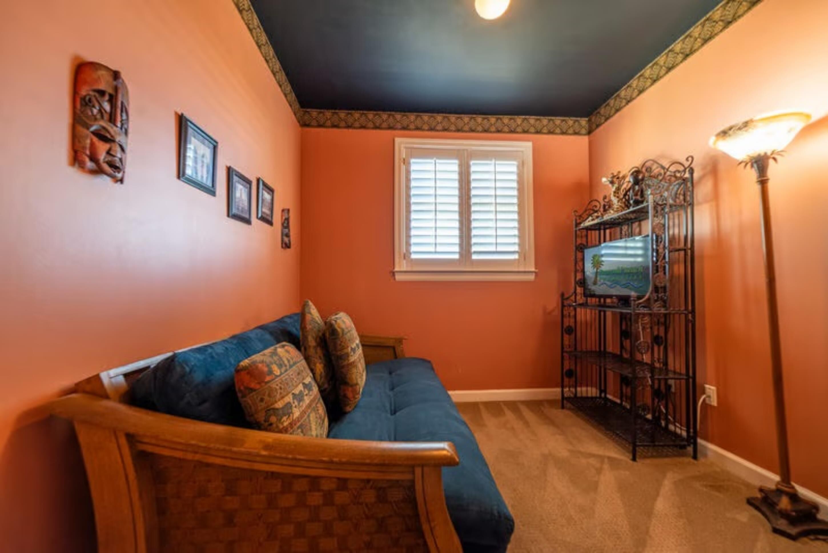 A room with a blue sofa, a wooden chair, a television on a black stand, and a floor lamp.