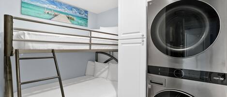 Una cama tipo litera con una escalera, una lavadora y un cuadro de un muelle.
