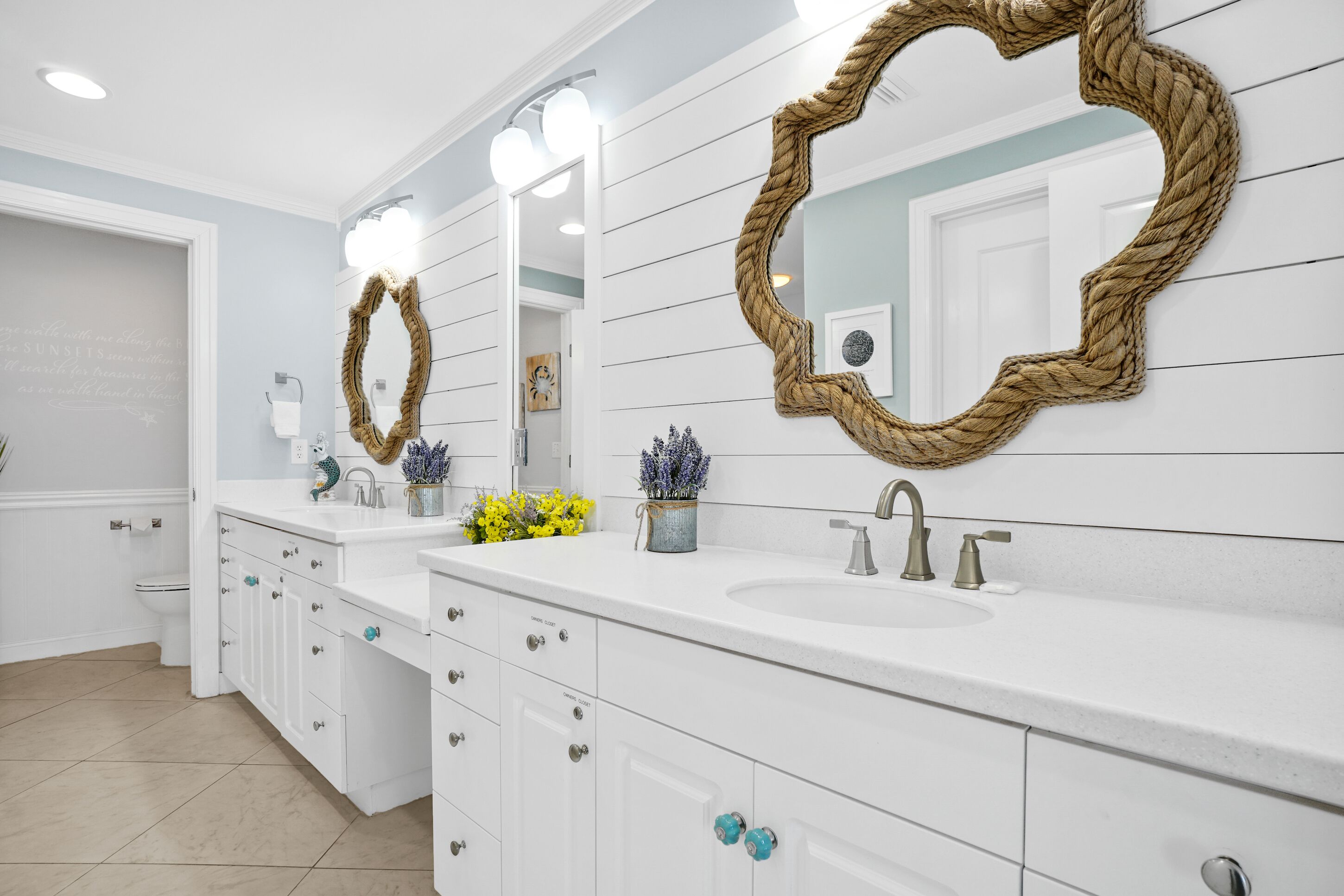 A modern bathroom with white cabinetry, two sinks, and decorative mirrors.