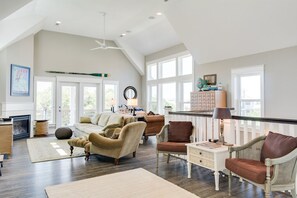 Uma sala de estar espaçosa com teto alto, janelas grandes e diversas opções de assentos, incluindo sofás e poltronas.