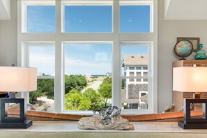 Ein Zimmer mit großen Fenstern, das einen Blick auf eine Straße und Gebäude bietet. An einem Holztisch stehen auf jeder Seite zwei Lampen und in der Mitte ein dekoratives Objekt.
