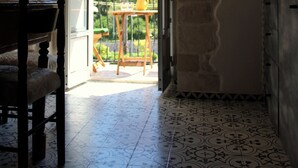 An interior space with a stone wall, a wooden chair, a tiled floor, and an open doorway leading to an outdoor area with a table and chairs.
