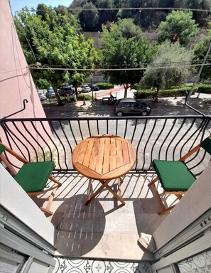 Ein Balkon mit einem Holztisch und zwei grünen Sitzgelegenheiten mit Polstern.