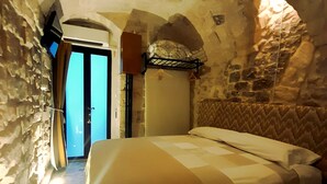 A bedroom with a stone wall, a bed, a hanging light fixture, and a door leading to another room.