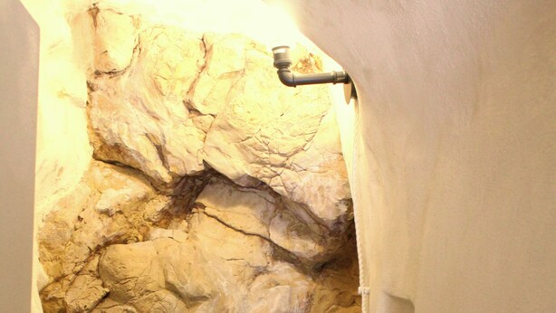 A bathroom with a rock wall, a bathtub, and a statue.