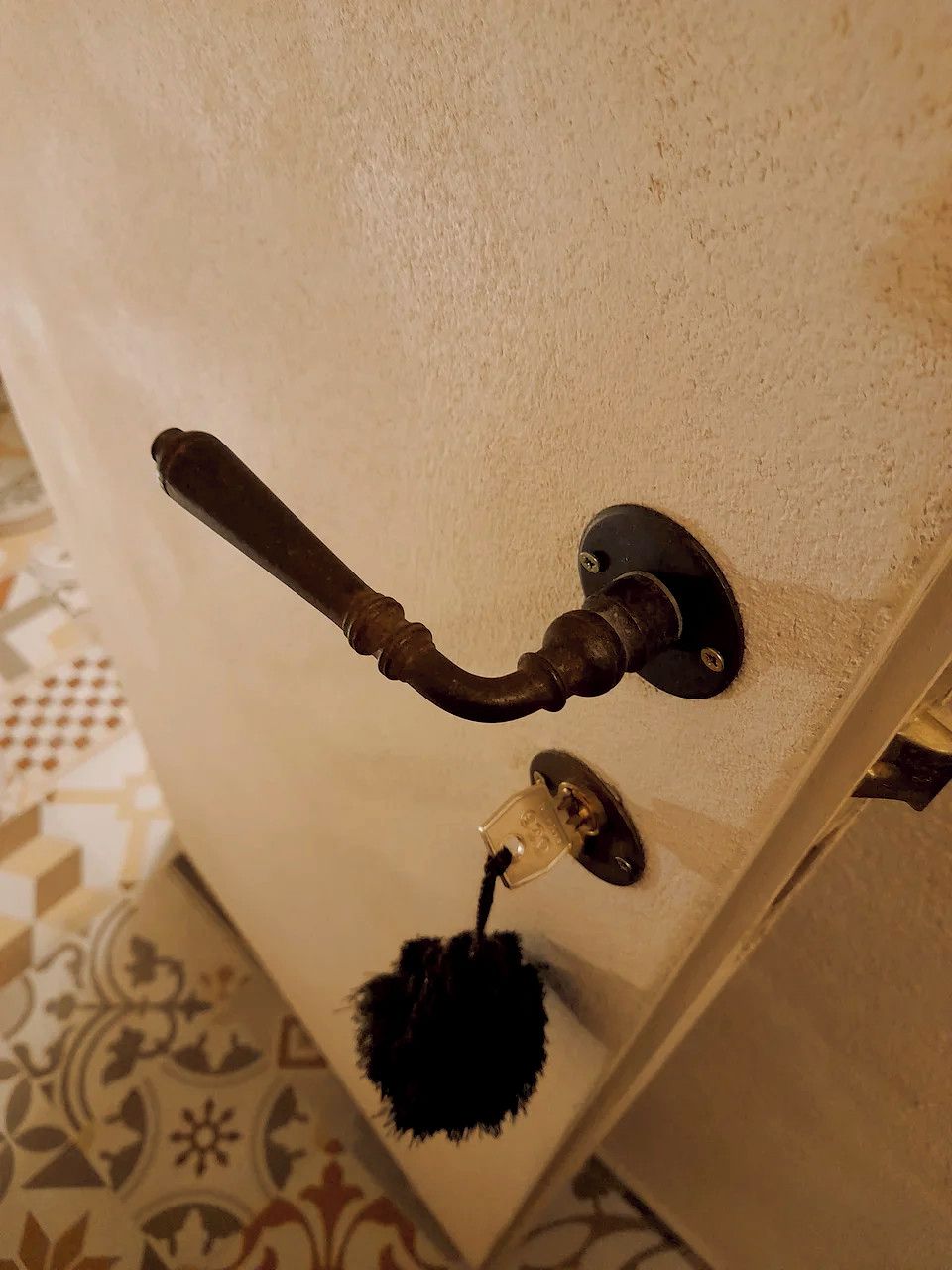 A door with a brass handle and a keyhole, and a keychain with a tassel hanging from it.