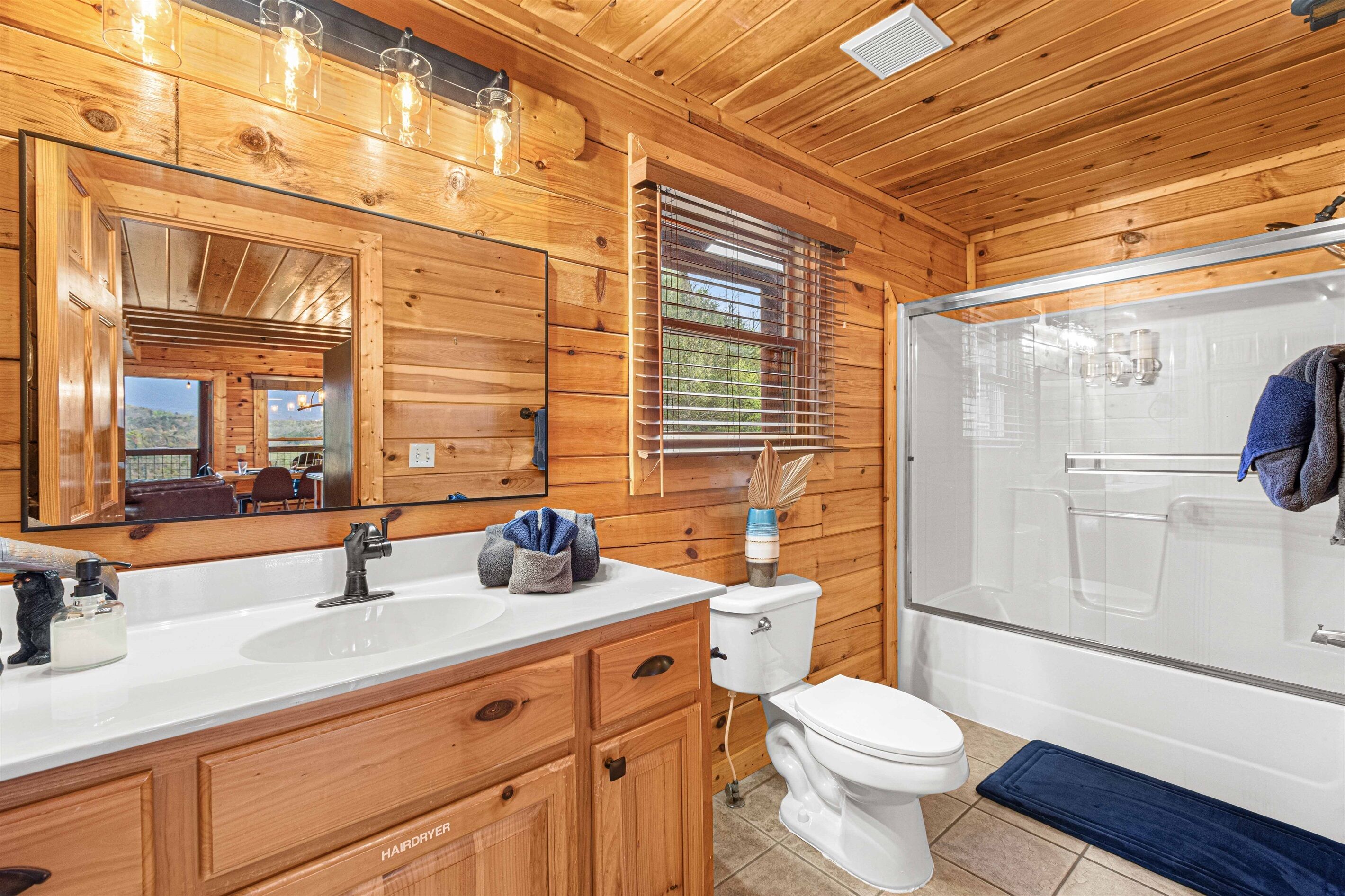 Ein Badezimmer einer Holzhütte mit einem großen Spiegel, zwei Waschbecken, einer Toilette und einer Duschkabine aus Glas.