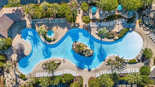 Vista aérea de un resort con varias piscinas, tumbonas y palmeras.
