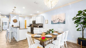 Una cocina moderna con gabinetes blancos, una isla central y un comedor con sillas blancas y una mesa de madera.