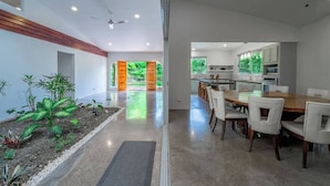 Une cuisine moderne avec des meubles blancs, un coin repas doté d’une table en bois et de chaises blanches, et une vue sur la verdure grâce à de grandes fenêtres.