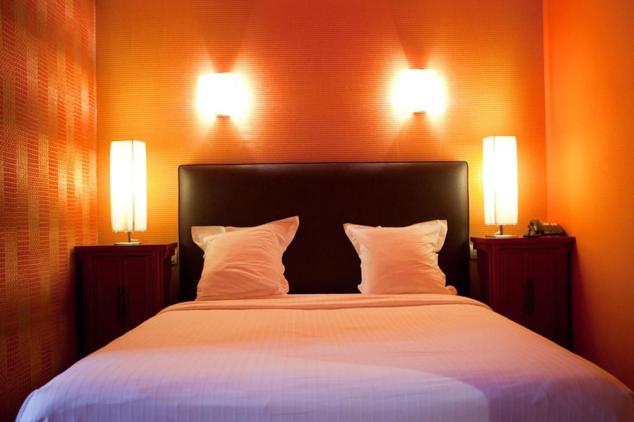 Habitación de hotel con una cama grande, dos lámparas de noche y una pared naranja con textura.