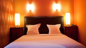 Habitación de hotel con una cama grande, dos lámparas de noche y una pared naranja con textura.