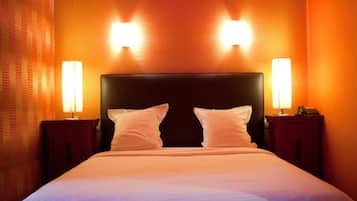 Habitación de hotel con una cama grande, dos lámparas de noche y una pared naranja con textura.