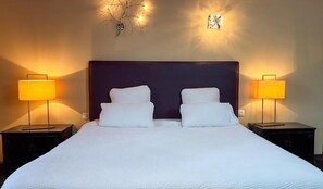 Un lit double avec du linge de lit blanc, deux tables de chevet avec des lampes, une tête de lit sombre et des appliques murales.