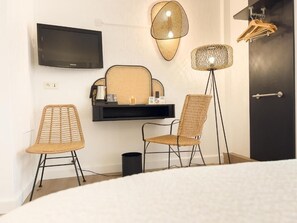 Habitación de hotel con televisor de pantalla plana, dos sillones de mimbre, una mesita con bandeja, una lámpara de pie y una puerta oscura.