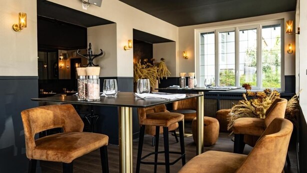 Un comedor moderno con una mesa de madera oscura, sillas de terciopelo y vistas a zonas verdes a través de amplios ventanales.